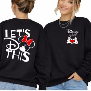 K&ouml;nnte beinhalten: Schwarze Sweatshirts mit Disney-Motiven. Eines zeigt "LET'S DO THIS" mit einem Minnie-Maus-Design und einer roten Schleife. Das andere zeigt "Disney Vibes" mit einer herzf&ouml;rmigen Handgeste und einem roten Herzen.