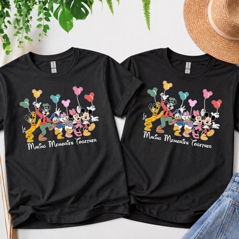 May include: Two black t-shirts with a colorful graphic of Disney characters holding balloons. The graphic includes Mickey Mouse, Minnie Mouse, Donald Duck, and Goofy. The text "Making Memories Together" is written below the characters.
