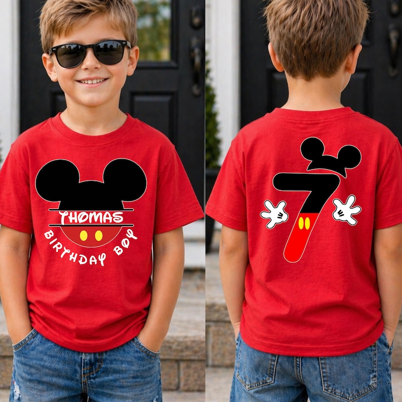 May include: Red t-shirt with a Mickey Mouse design. The front of the shirt has the text "THOMAS BIRTHDAY BOY" and a Mickey Mouse head. The back of the shirt has a number 7 with Mickey Mouse gloves and head.