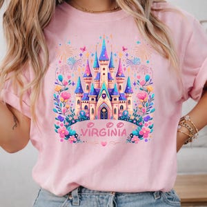 K&ouml;nnte beinhalten: Hellrosa Sweatshirt mit einem farbenfrohen Schloss-Motiv mit blauen, rosa und lila T&uuml;rmen. Das Wort "VIRGINIA" ist darunter gedruckt, umgeben von floralen und Feuerwerks-Designs. Ein skurriles Design f&uuml;r ein Reise- oder Souvenir-Thema.