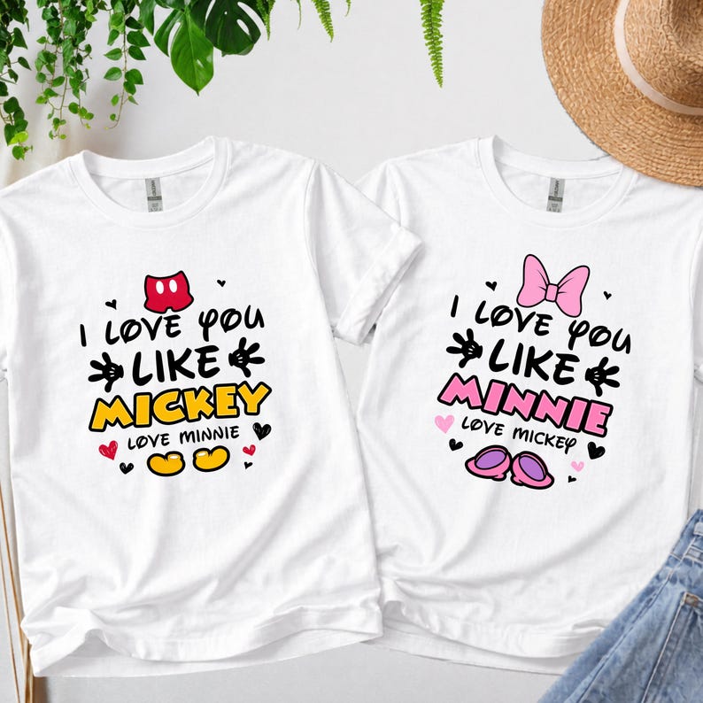 Pode incluir: Duas camisetas brancas com gr&aacute;ficos correspondentes. Uma camisa diz "I love you like Mickey" com um la&ccedil;o vermelho e detalhes do Mickey Mouse. A outra diz "I love you like Minnie" com um la&ccedil;o rosa e detalhes da Minnie Mouse.