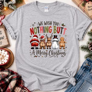 May include: A heather gray crew neck t-shirt featuring a graphic of Santa Claus, a bear, a reindeer, a snowman, and a gingerbread man facing away with their backsides exposed. The text reads WE WISH YOU NOTHING BUTT A Merry Christmas.
