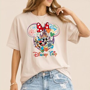 Puede incluir: Camiseta beige con un gr&aacute;fico colorido de Disney. El dise&ntilde;o incluye el lazo de Minnie Mouse, un castillo y varios personajes de Disney. Tambi&eacute;n se ven las palabras "Best Day Ever" y "Disney Trip".
