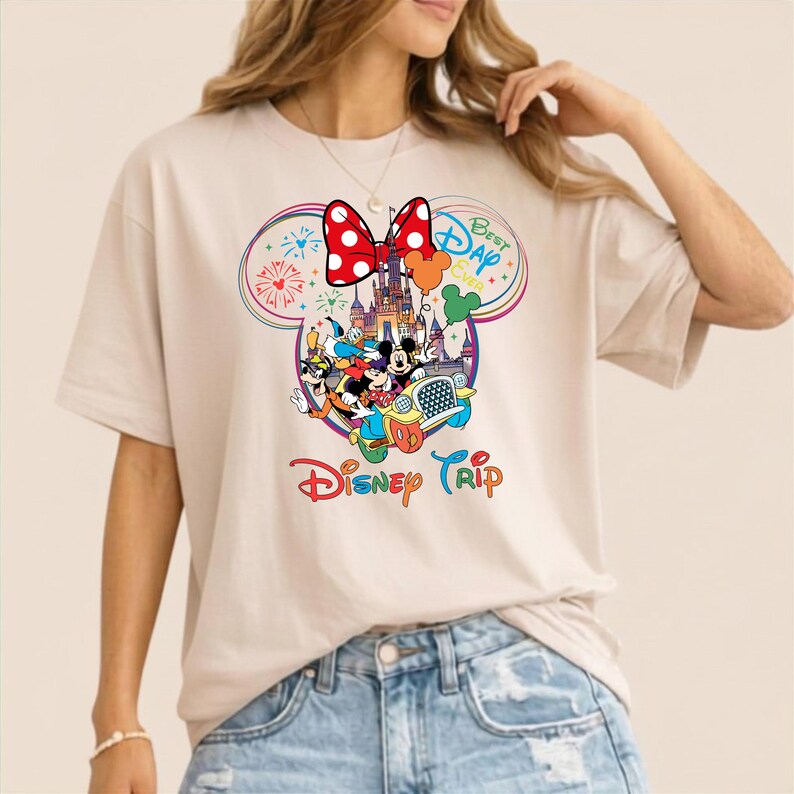 Puede incluir: Camiseta beige con un gr&aacute;fico colorido de Disney. El dise&ntilde;o incluye el lazo de Minnie Mouse, un castillo y varios personajes de Disney. Tambi&eacute;n se ven las palabras "Best Day Ever" y "Disney Trip".