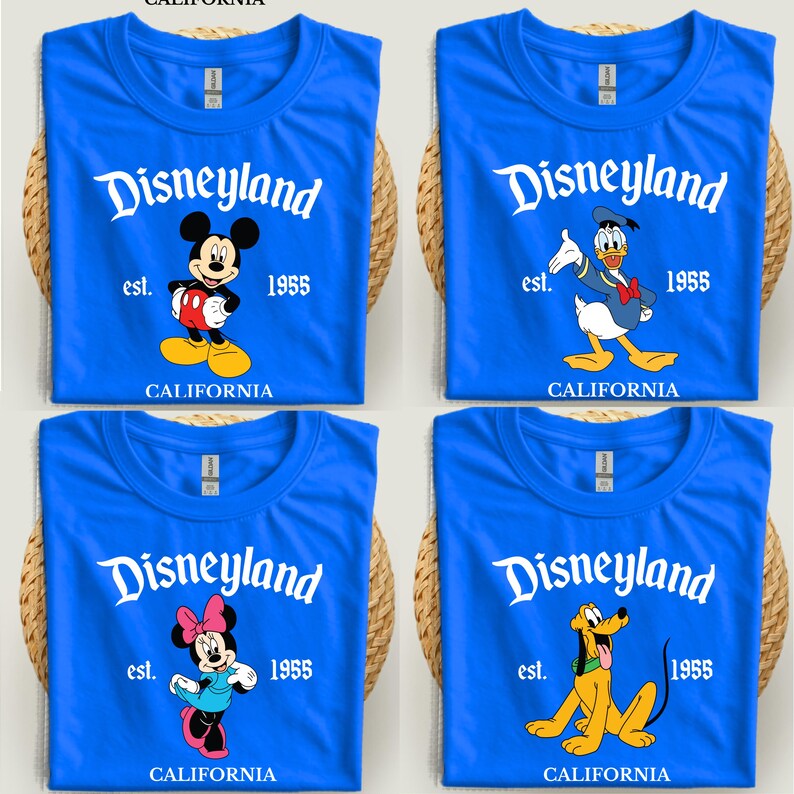 Op de afbeelding: Vier blauwe T-shirts met het Disneyland-logo en tekenfilmfiguren: Mickey Mouse, Donald Duck, Minnie Mouse en Pluto. Elk shirt heeft de tekst "est. 1955 CALIFORNIA".
