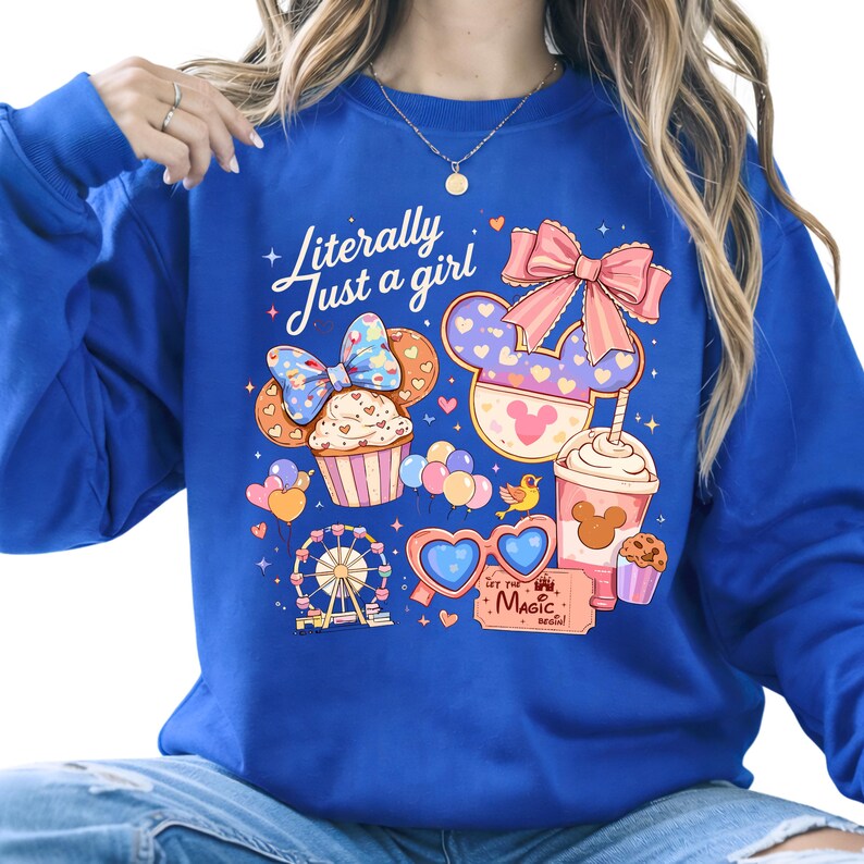 Pode incluir: Camisola azul royal com um design gr&aacute;fico colorido. O design inclui um cupcake, um la&ccedil;o, uma bebida e uma roda gigante. O texto na camisola diz "Literally Just a girl" e "Let the Magic Begin!"
