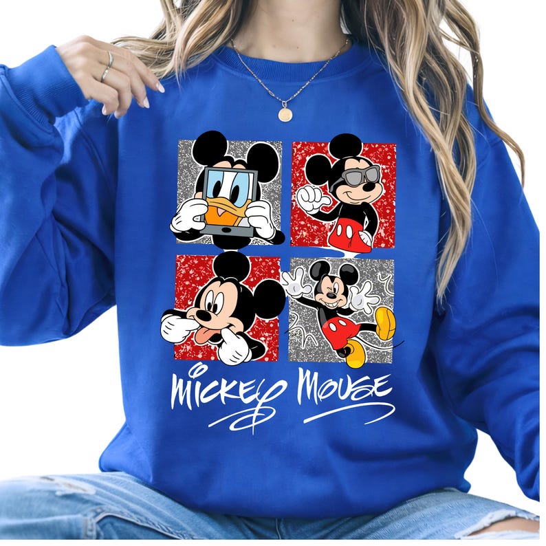 Op de afbeelding: Koning blauwe sweatshirt met een vier-paneel ontwerp met Mickey Mouse in verschillende poses. Elk paneel heeft een rode of zilveren glitter achtergrond. De woorden "Mickey Mouse" staan eronder in witte letters.