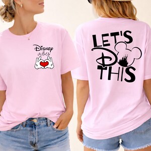 K&ouml;nnte beinhalten: Rosa T-Shirts mit Disney-Motiven. Ein Shirt zeigt "Disney Vibes" mit Mickey Mouse-H&auml;nden, die ein Herz formen. Das andere Shirt hat "Let's do this" mit einer Mickey Mouse-Silhouette und einem Schloss.