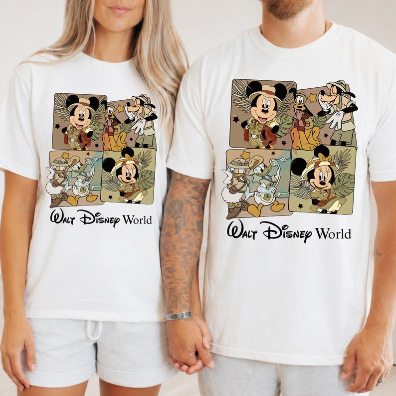 Puede incluir: Camisetas blancas con un gr&aacute;fico colorido de Mickey y Minnie Mouse, Goofy y Donald Duck con trajes de safari. El texto "Walt Disney World" est&aacute; impreso debajo del gr&aacute;fico en escritura negra.