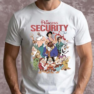 May include: White t-shirt with a colourful graphic of Disney characters such as the Beast, Aladdin, and Olaf. The text "Princess Security Club" is printed in red above the characters.