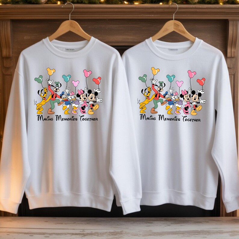 May include: Two white sweatshirts with a colorful graphic of Disney characters, including Mickey and Minnie Mouse, Donald and Daisy Duck, and Goofy. The characters are holding heart-shaped balloons. The text "Making Memories Together" is printed below the graphic.