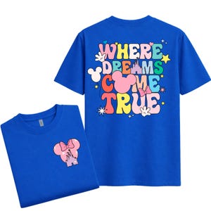 May include: Two royal blue t-shirts. One shirt features a pink Minnie Mouse head graphic with a castle and bow. The other shirt displays the words "WHERE DREAMS COME TRUE" in colourful bubble letters, with Mickey Mouse hands, stars, and a castle.