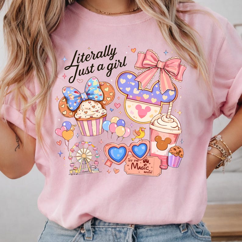 Pode incluir: Camisola rosa claro com um design gr&aacute;fico colorido. O design inclui um cupcake, orelhas do Mickey, uma bebida e uma roda gigante. O texto "Literally Just a girl" est&aacute; escrito em it&aacute;lico. O design inclui cora&ccedil;&otilde;es, la&ccedil;os e a frase "Let the Magic Begin!"