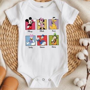 May include: White baby bodysuit featuring six Disney characters: Mickey, Minnie, Pluto, Daisy, Donald, and Goofy, each in a colorful square. The characters' names are printed below their images. The bodysuit has short sleeves and snap closures.
