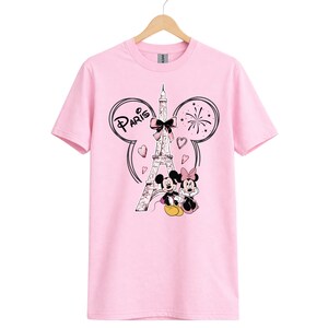K&ouml;nnte beinhalten: Hellrosa T-Shirt mit einem Aufdruck von Mickey und Minnie Mouse vor dem Eiffelturm in Paris. Das Design enth&auml;lt das Wort "Paris" und Herzen.