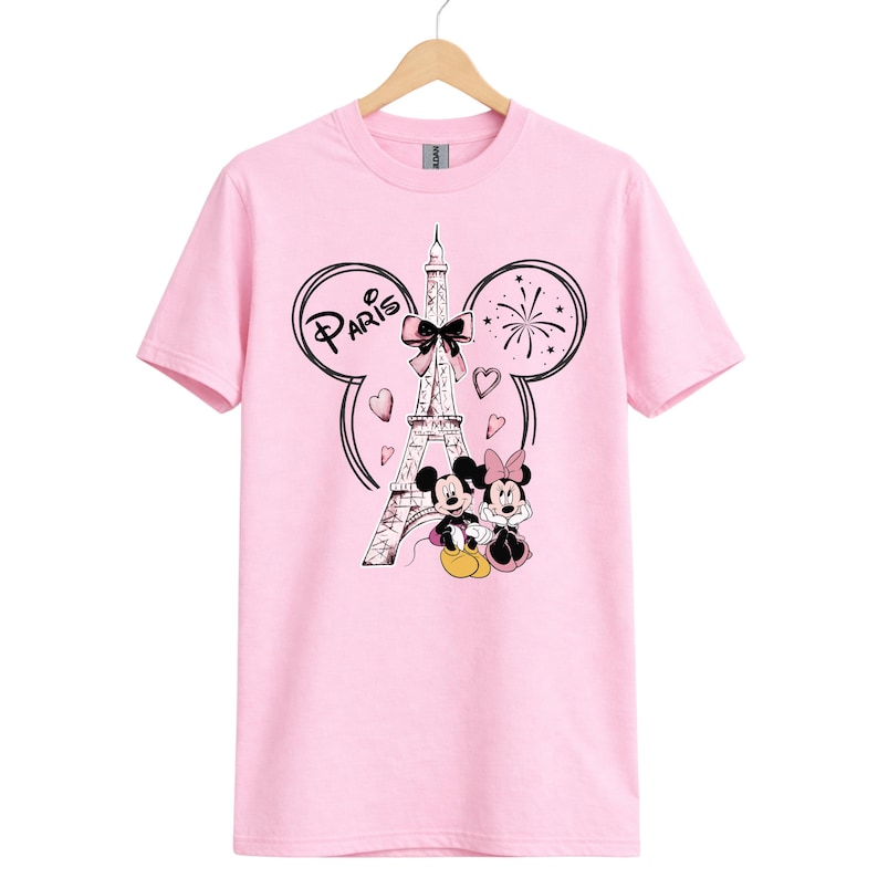 K&ouml;nnte beinhalten: Hellrosa T-Shirt mit einem Aufdruck von Mickey und Minnie Mouse vor dem Eiffelturm in Paris. Das Design enth&auml;lt das Wort "Paris" und Herzen.