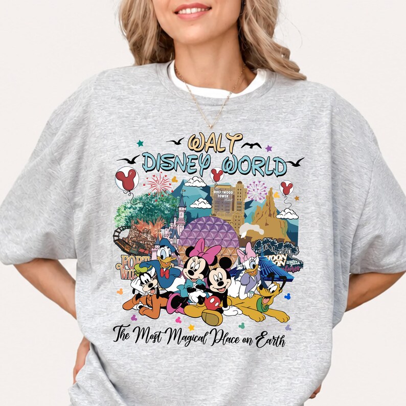 K&ouml;nnte beinhalten: Ein hellgraues Sweatshirt mit einer farbenfrohen Grafik von Disney-Figuren und Wahrzeichen. Das Design zeigt Micky und Minnie Maus, Donald Duck und Goofy, mit dem Text "Walt Disney World" und "The Most Magical Place on Earth."