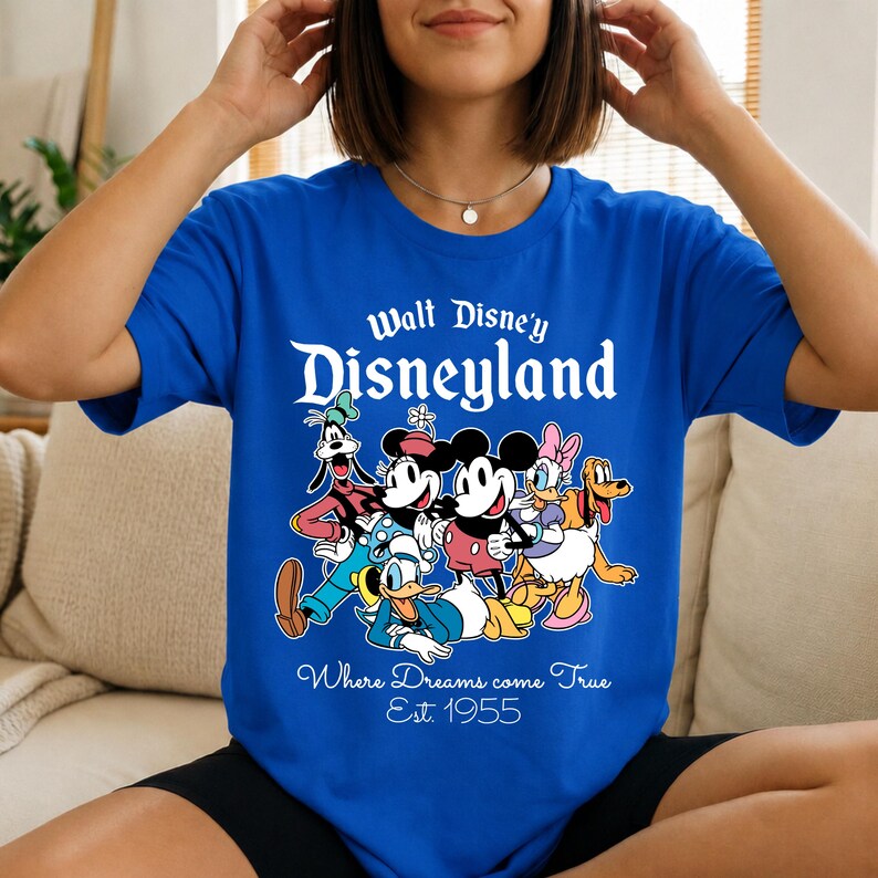 Pu&ograve; includere: T-shirt blu reale con una grafica dei personaggi Disney, tra cui Topolino e Minnie, Paperino, Pippo e Paperina. Il testo "Walt Disney's Disneyland" e "Where Dreams come True Est. 1955" sono stampati sulla maglietta.