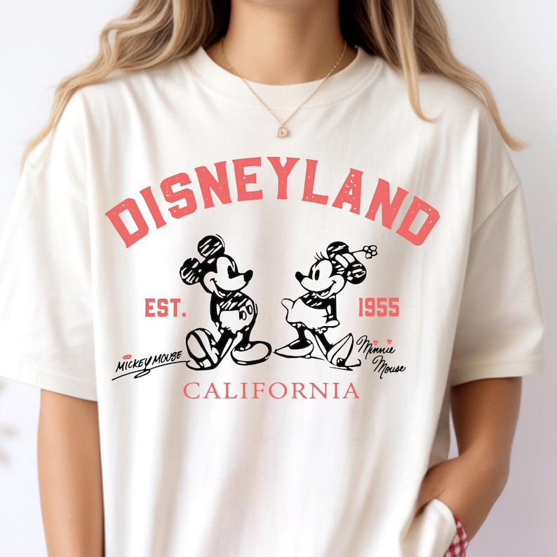 Puede incluir: Camiseta de color crema con un gr&aacute;fico vintage de Disneyland. El dise&ntilde;o incluye a Mickey y Minnie Mouse, el texto "DISNEYLAND" en rojo y el a&ntilde;o "1955". El texto adicional incluye "Mickey Mouse" y "Minnie Mouse".