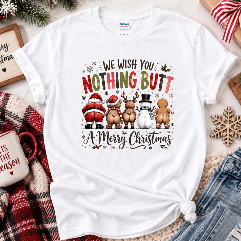 May include: A white short-sleeve t-shirt featuring a graphic of Santa Claus, a bear, a reindeer, a snowman, and a gingerbread person facing away. The text reads: WE WISH YOU NOTHING BUTT A MERRY CHRISTMAS, decorated with small snowflakes and holly.