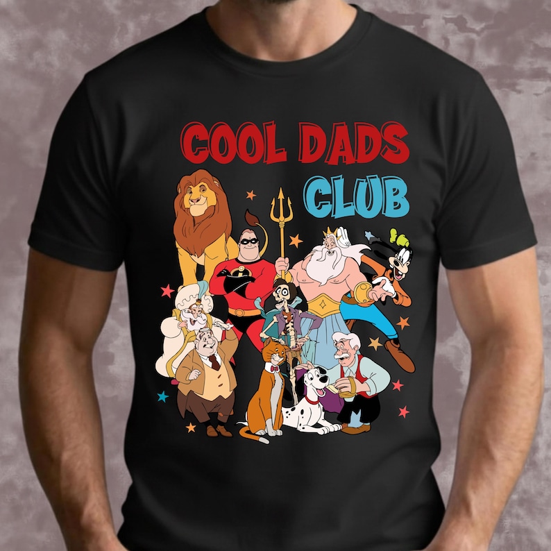 May include: Black t-shirt with a colorful graphic of cartoon characters and the text "COOL DADS CLUB" in red and blue. The graphic includes a lion, superhero, and other animated figures.