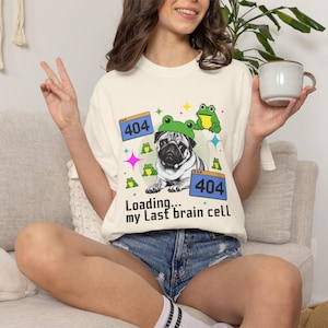 May include: Cream-colored t-shirt featuring a pug wearing a frog hat, surrounded by frog and star graphics. The text "Loading... my Last brain cell" and two "404" error messages are also printed on the shirt.