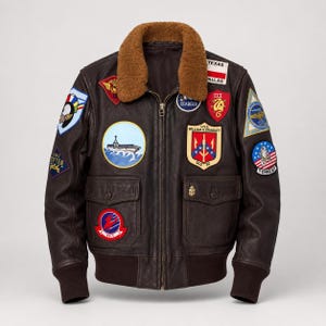 Könnte beinhalten: Eine dunkelbraune Lederfliegerjacke mit braunem Lammfellkragen, Frontreißverschluss und gerippten Bündchen. Die Jacke ist mit zahlreichen bunten gestickten Aufnähern verziert, darunter ein Schiff, eine Texas-Flagge und verschiedene militärische Abzeichen.