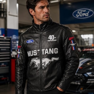 Könnte beinhalten: Eine schwarze Lederjacke mit durchgehendem Frontreißverschluss und Stehkragen. Auf der Brust steht das Wort MUSTANG in weißen Buchstaben über einem großen weißen galoppierenden Pferdelogo. Sie enthält ein Ford-Logo, 40th Anniversary und GT-Embleme.
