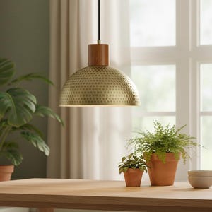 May include: A pendant light with a wooden top and a textured, gold-colored shade hangs above a wooden table. Potted plants, including ferns and a large-leafed plant, sit on the table. The background includes a window and curtains.