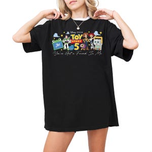 Puede incluir: Una camiseta negra de manga corta con un estampado gr&aacute;fico de los personajes de Disney Pixar Toy Story 5, incluyendo a Buzz Lightyear, Woody y Jessie. El texto dice Toy Story 5 y You've Got a Friend In Me con peque&ntilde;as estrellas amarillas.