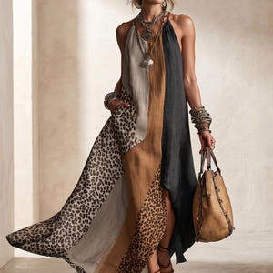 May include: A halter-neck maxi dress with a color-block design featuring leopard print, gray, tan, and black panels. The dress is paired with a brown leather handbag and strappy sandals. The model is wearing layered necklaces and bracelets.