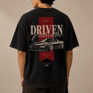 May include: A black short-sleeve t-shirt featuring a graphic on the back. The design includes a red vertical banner, the text "DRIVEN Collective," and a detailed illustration of a sports car. Additional text includes "TOKYO, JAPAN" and "EST 2019."