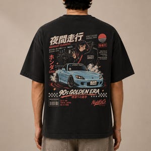 Puede incluir: Una camiseta negra de manga corta con un estampado gráfico en la espalda. El diseño incluye un coche deportivo azul claro, una persona en el asiento del conductor, texto en japonés y las palabras Midnight Runners, 90s Golden Era y NightKoiCo.
