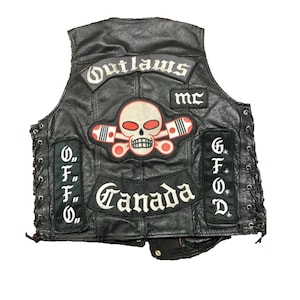 May include: A black leather vest featuring multiple patches, including a central skull and cross-piston emblem, the text Outlaws MC, Canada, and vertical side patches with the letters O.F.F.O. and G.F.O.D. The vest has side lacing details.