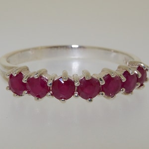May include: A silver band ring with seven red ruby stones set in a prong setting.