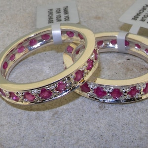Può includere: Due anelli d'argento con una fila di pietre preziose rosa attorno alla fascia. Gli anelli sono impilati uno sopra l'altro.
