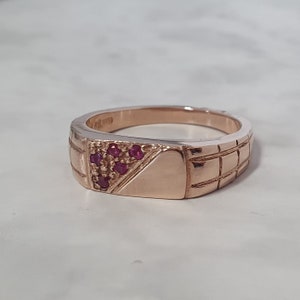 May include: A gold ring with a textured band and a small triangle of red gemstones.