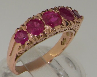May include: A rose gold ring featuring five oval-cut rubies. The ring has an ornate, floral design on the band and around each gemstone. The rubies are a vibrant, deep red color, and the ring is set against a neutral background.