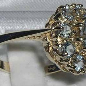 Pode incluir: Um anel de ouro com um grupo de pedras preciosas azuis claras engastadas em um design floral.