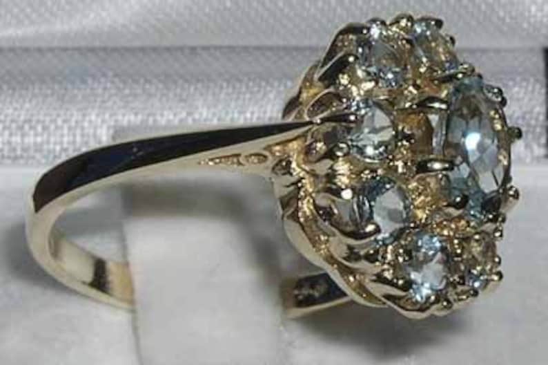 Pode incluir: Um anel de ouro com um grupo de pedras preciosas azuis claras engastadas em um design floral.