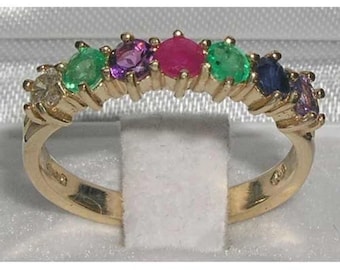 May include: A gold ring featuring a row of colorful gemstones. The gemstones include emerald green, amethyst purple, ruby red, and sapphire blue. The ring is set on a gold band.
