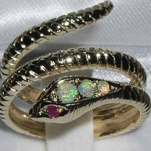 以下が含まれることがあります： 3つのオパールとルビーのアクセントが付いた金の蛇のリング。蛇はリングのバンドに巻き付けられています。