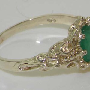May include: A silver ring with an ornate design featuring a large, oval-shaped emerald gemstone.