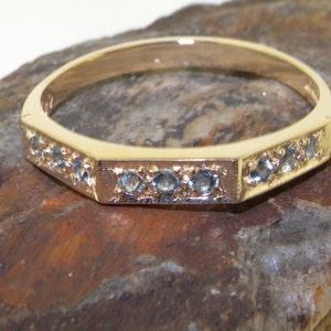 May include: A gold band ring with a row of small, light blue gemstones set in a hexagonal shape.