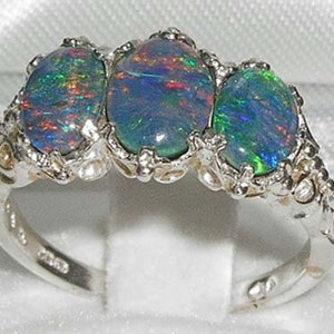 May include: A silver ring with three oval-shaped opal gemstones. The opals are a mix of blue, green, and red.