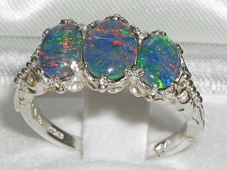 May include: A silver ring with three oval-shaped opal gemstones. The opals are a mix of blue, green, and red.