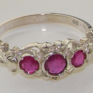 May include: A silver ring with three pink gemstones set in a floral design.