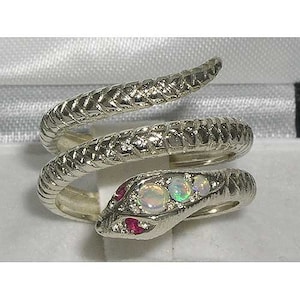 以下が含まれることがあります： 銀色のヘビの指輪。ヘビの頭には3つのオパールと2つの赤い石が飾られています。指輪は白い背景に置かれています。