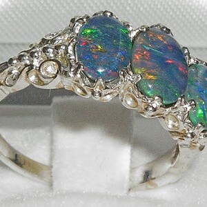 May include: A silver ring with three oval-shaped opals. The opals are a mix of blue, green, and black.