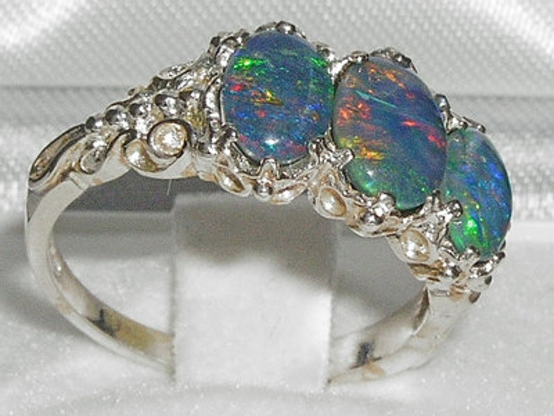May include: A silver ring with three oval-shaped opals. The opals are a mix of blue, green, and black.